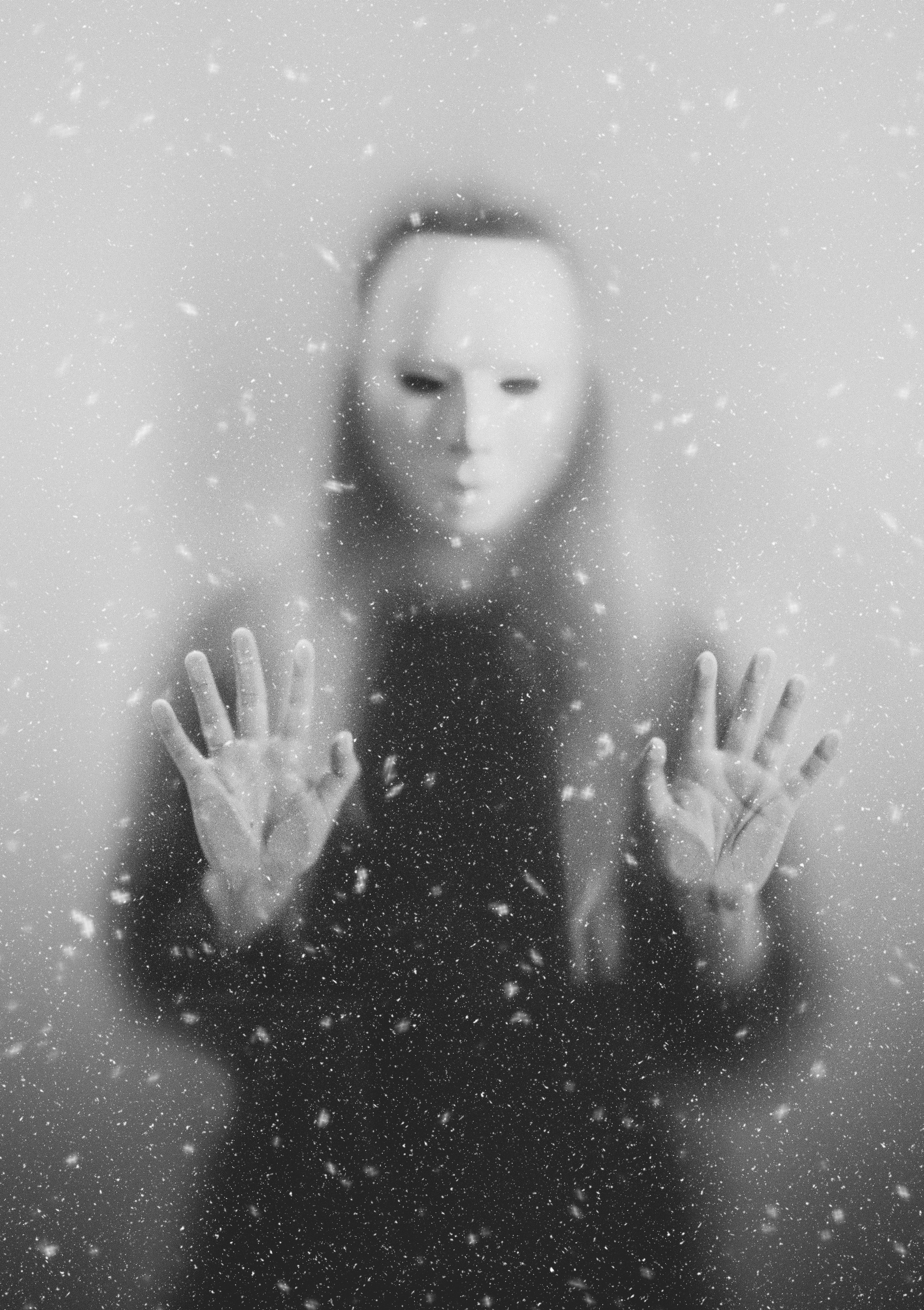 uma mulher com as mãos na frente do rosto, com uma máscara branca; foto preta e branca